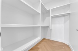 Custom closet system featuring white built-in shelving, hanging rods, and wood-finish herringbone flooring - 