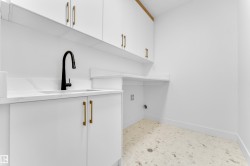 Laundry room featuring white cabinetry with brass hardware, a built-in sink with a matte black faucet, light-toned countertop, and terrazzo-style flooring - 
