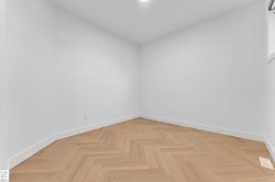 Room featuring light wood-finish flooring with a herringbone pattern, crisp white walls, and bright overhead lighting - 