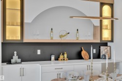 Built-in cabinetry featuring illuminated arched glass-front display cabinets, an open wood shelf, and solid lower cabinets with gold-tone hardware - 