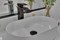 Vessel sink with ribbed ceramic exterior, complemented by a bronze-finish waterfall faucet and a white countertop featuring subtle veining - 
