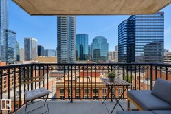 Private balcony featuring an ornate black metal railing, concrete flooring, and a backdrop of contemporary high-rise buildings - 