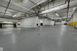 Spacious underground parking facility featuring concrete walls, exposed ceiling pipes, and overhead fluorescent lighting - 