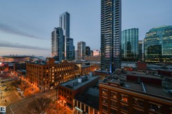 Urban skyline featuring numerous high-rise buildings with contemporary glass and steel facades, alongside lower-rise brick structures with illuminated windows - 