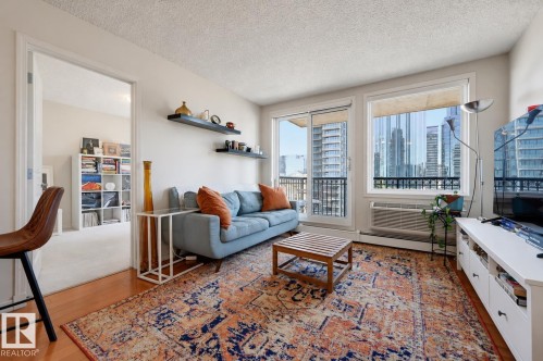 Living area featuring wood-finish flooring, a full-height glass sliding door, and an expansive window with city architecture visible - 1103 10180 104 Street, Edmonton, AB 