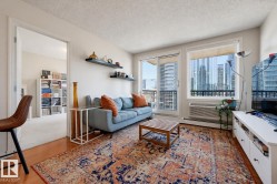Living area featuring wood-finish flooring, a full-height glass sliding door, and an expansive window with city architecture visible - 