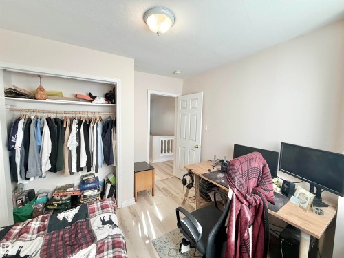 Room featuring light-toned walls, wood-finish flooring, a built-in closet with shelving and hanging storage, a ceiling-mounted light fixture, and a paneled interior door - 11941 78 Street, Edmonton, AB 