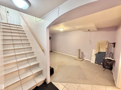 Tiled staircase with wood handrail, recessed ceiling light, and arched doorway leading to a carpeted room with a flush-mount light fixture - 11941 78 Street, Edmonton, AB 