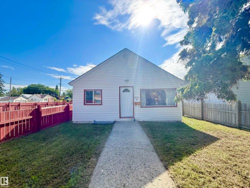 White siding exterior with a pitched roofline, bordered by a red privacy fence - 11941 78 Street, Edmonton, AB 