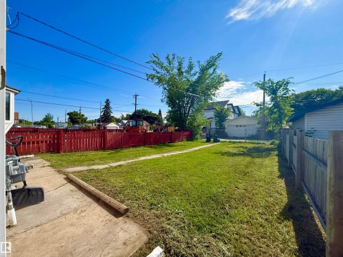 Expansive grassy backyard featuring a red wooden fence, concrete patio, and mature trees - 11941 78 Street, Edmonton, AB 