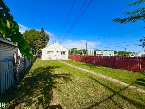 Spacious backyard featuring a manicured lawn, a paved pathway, and a red privacy fence - 11941 78 Street, Edmonton, AB 