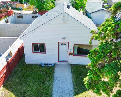 White siding exterior with a pitched roof, featuring a front door with an arched window insert - 11941 78 Street, Edmonton, AB 