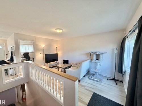 Upper-level living area featuring wood-finish flooring, a white spindle railing with a natural wood-tone cap, light-colored walls, and a ceiling-mounted light fixture - 11941 78 Street, Edmonton, AB 