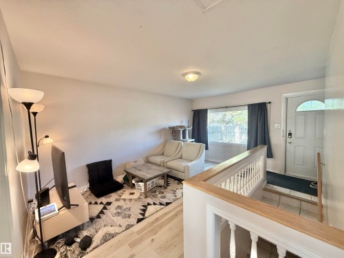 Living area featuring wood-finish flooring, a white paneled entry door with an arched window, and a white balustrade with a light wood-finish handrail - 11941 78 Street, Edmonton, AB 