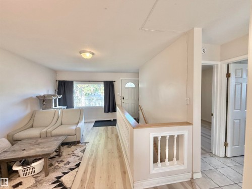 Light wood-finish flooring extending through the living area, complemented by a white-painted stair rail with decorative balusters - 11941 78 Street, Edmonton, AB 
