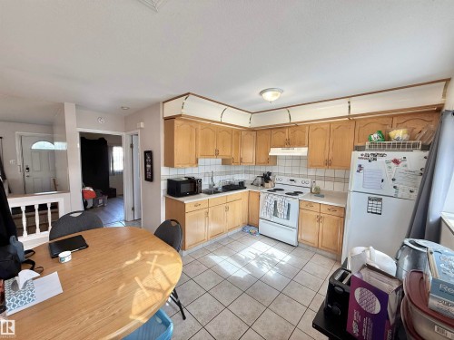 Kitchen featuring light wood cabinetry, white tile backsplash, and white tile flooring - 11941 78 Street, Edmonton, AB 