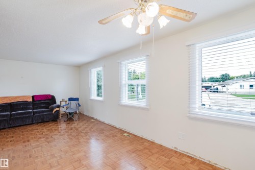 Spacious living area featuring wood-finish parquet flooring, multiple windows with blinds, a textured ceiling, and an overhead ceiling fan with integrated lighting - 212 Homestead Crescent, Edmonton, AB 