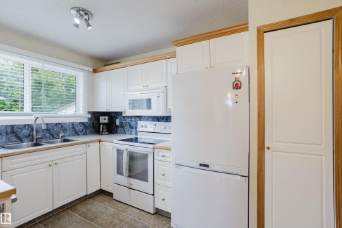 Kitchen featuring white cabinetry with gold-toned hardware, laminate countertops, and a dual-basin stainless steel sink - 212 Homestead Crescent, Edmonton, AB 