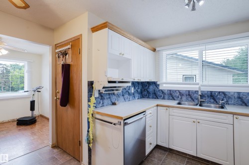 Kitchen featuring white cabinetry, a dual basin stainless steel sink, a stainless steel dishwasher, and a blue patterned backsplash - 212 Homestead Crescent, Edmonton, AB 