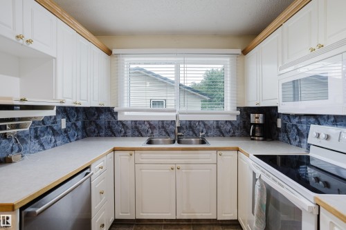 U-shaped kitchen featuring white cabinetry, light countertops, a double-basin stainless steel sink, a dishwasher, and a built-in microwave - 212 Homestead Crescent, Edmonton, AB 