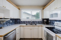U-shaped kitchen featuring white cabinetry, light countertops, a double-basin stainless steel sink, a dishwasher, and a built-in microwave - 