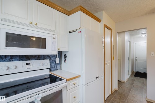 Kitchen featuring white cabinetry with gold-toned hardware, coordinating white appliances, and a dark tile backsplash - 212 Homestead Crescent, Edmonton, AB 
