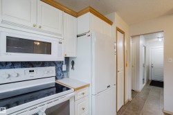 Kitchen featuring white cabinetry with gold-toned hardware, coordinating white appliances, and a dark tile backsplash - 