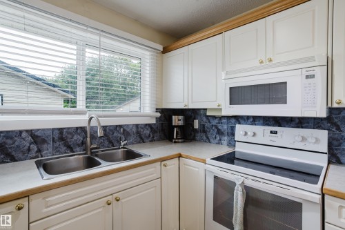 Kitchen featuring white cabinetry with gold-toned hardware, a double basin stainless steel sink with a gooseneck faucet, light-toned countertops, and a tile backsplash - 212 Homestead Crescent, Edmonton, AB 