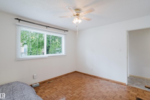 Bright room featuring a large window with white blinds, wood-finish parquet flooring, and a ceiling fan with integrated lighting - 212 Homestead Crescent, Edmonton, AB 