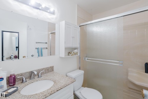 Bathroom featuring a vanity with an undermount sink and stone countertop, mirrored wall with vanity lighting, wall-mounted storage cabinet, and a shower enclosure with frosted glass sliding doors - 212 Homestead Crescent, Edmonton, AB 