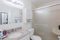 Bathroom featuring a vanity with an undermount sink and stone countertop, mirrored wall with vanity lighting, wall-mounted storage cabinet, and a shower enclosure with frosted glass sliding doors - 