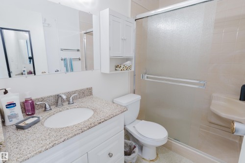 Bathroom featuring a vanity with a granite-style countertop and undermount sink, chrome fixtures, a mirrored medicine cabinet, and a shower enclosure with a sliding frosted glass door - 212 Homestead Crescent, Edmonton, AB 