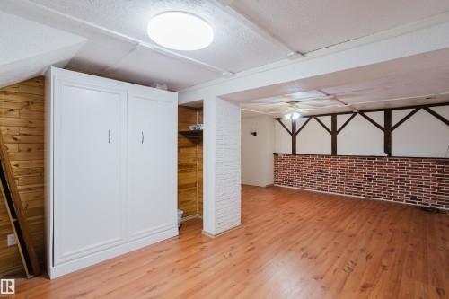 Spacious interior featuring wood-finish flooring, a built-in white cabinet, and a brick accent wall with exposed beam detailing - 212 Homestead Crescent, Edmonton, AB 