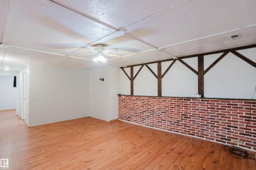 Spacious room featuring wood-finish flooring, a ceiling fan with integrated lighting, and a partial brick-patterned wall - 212 Homestead Crescent, Edmonton, AB 