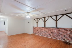 Spacious room featuring wood-finish flooring, a ceiling fan with integrated lighting, and a partial brick-patterned wall - 