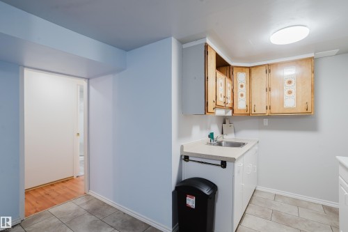 Dedicated utility area featuring a stainless steel sink, wood-finish upper cabinetry, and white base cabinetry - 212 Homestead Crescent, Edmonton, AB 
