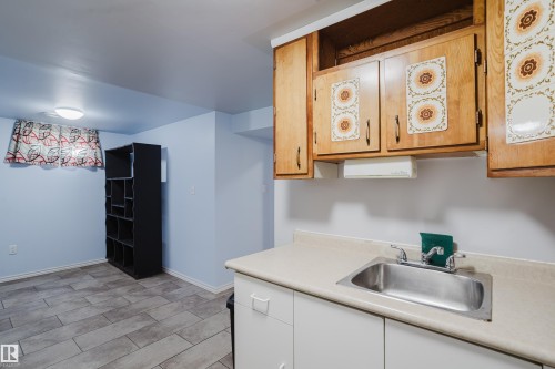 Kitchenette featuring wood-finish cabinetry with decorative panels, a stainless steel sink, and light-toned countertops - 212 Homestead Crescent, Edmonton, AB 