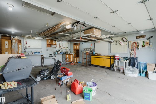 Spacious garage featuring a concrete floor, overhead lighting, garage door, built-in cabinetry, and wall-mounted shelving - 212 Homestead Crescent, Edmonton, AB 