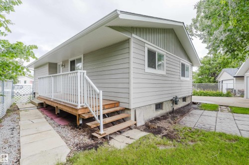 Exterior featuring light gray horizontal siding, a wood-finish deck with white railings, a concrete foundation, and a partial grass lawn with stepping stones - 212 Homestead Crescent, Edmonton, AB 