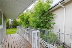 Covered wooden deck with white railing, overlooking a fenced yard with mature trees - 