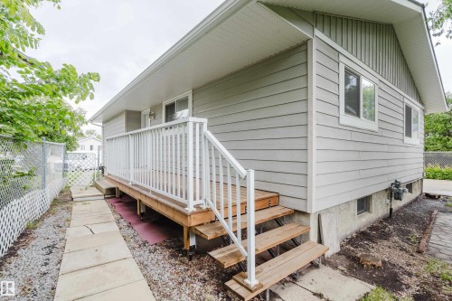 Side exterior featuring a raised wooden deck with white railings, wood-finish stairs, light-toned horizontal siding, and multiple windows - 212 Homestead Crescent, Edmonton, AB 