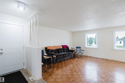 Entryway with tiled flooring opening to a living area featuring parquet wood-finish flooring, white walls, and two windows with blinds - 212 Homestead Crescent, Edmonton, AB 