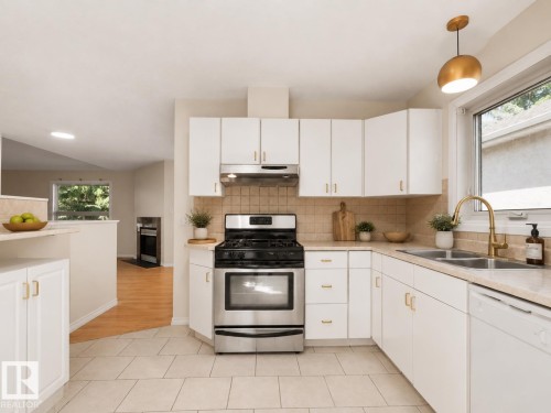 Kitchen featuring white cabinetry with gold-toned hardware, a stainless steel range with overhead ventilation, and a double basin sink with a gold-toned faucet - 1855 Mill Woods Rd E Nw, Edmonton, AB 