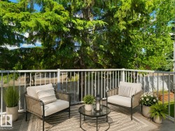 Private outdoor balcony featuring a white railing, a dark grey composite deck, and mature trees - 