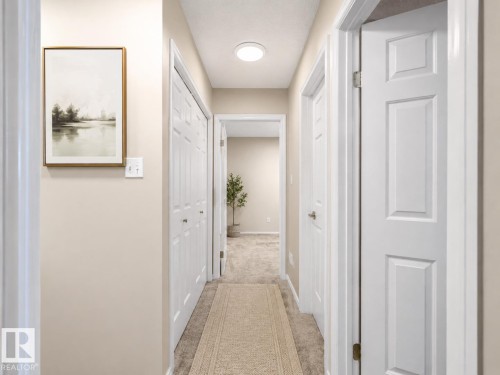 Carpeted hallway featuring a flush-mount ceiling light, white panel doors, and neutral-toned walls - 1855 Mill Woods Rd E Nw, Edmonton, AB 