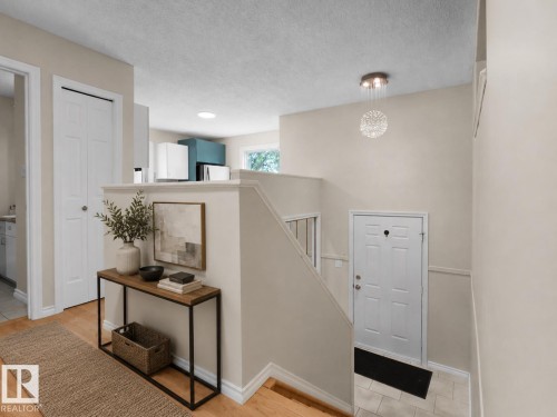 Foyer featuring light-toned walls, wood-finish flooring, a contemporary chandelier, and a white paneled door - 1855 Mill Woods Rd E Nw, Edmonton, AB 