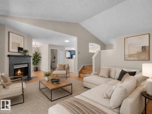 Spacious living area featuring a dark stone fireplace with a metal insert, light wood-finish flooring, and a vaulted ceiling - 1855 Mill Woods Rd E Nw, Edmonton, AB 