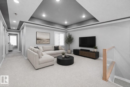 Spacious living area featuring a tray ceiling with recessed lighting, light grey carpeting, and a wood-finish media console - 714 Ebbers Place, Edmonton, AB 