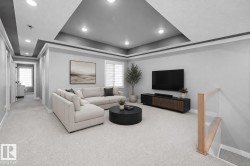 Spacious living area featuring a tray ceiling with recessed lighting, light grey carpeting, and a wood-finish media console - 