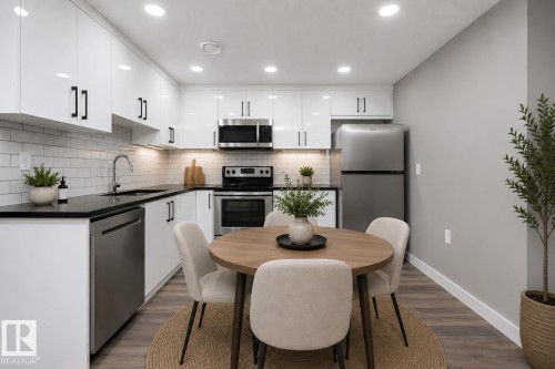 Modern kitchen featuring white cabinetry, black countertops, stainless steel appliances, white subway tile backsplash, and wood-finish flooring - 714 Ebbers Place, Edmonton, AB 